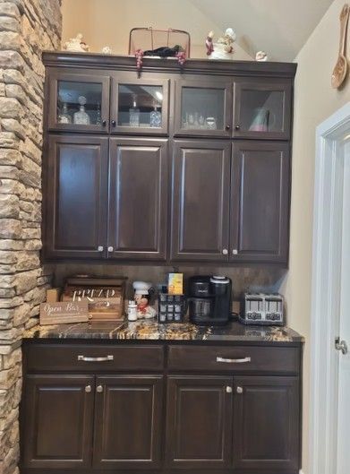 Dark wood kitchen cabinets with glass doors, countertop appliances, and a stone wall on the left.