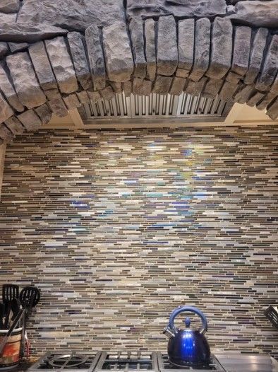 Kitchen backsplash with a blue kettle on the stove beneath a stone arch and textured tile wall