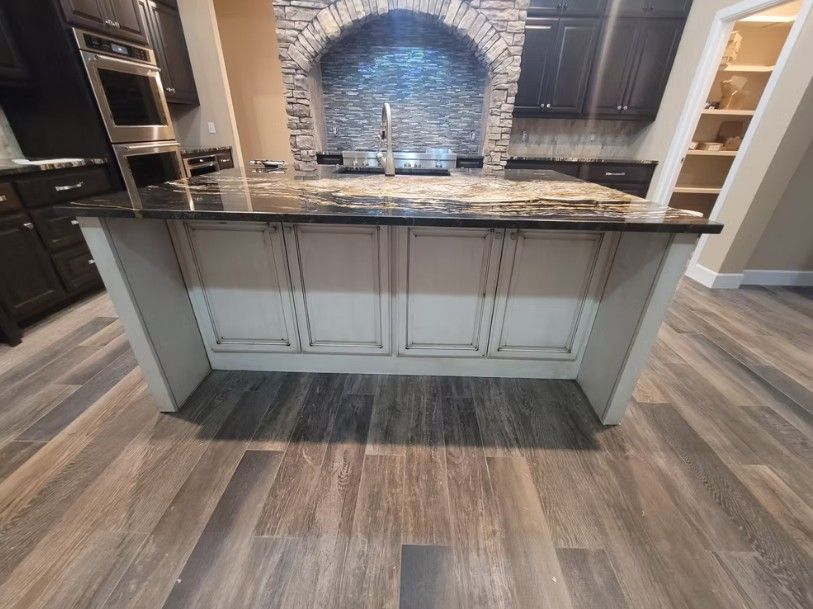 Kitchen island with dark countertop, white cabinets, and wood-look flooring in a modern kitchen