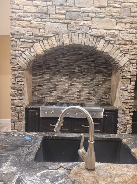 Stone fireplace with arched alcove above a dark kitchen sink and silver faucet.