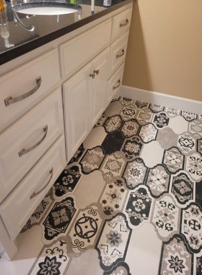Kitchen floor with black, white, and beige patterned tile beside white cabinets and sink.