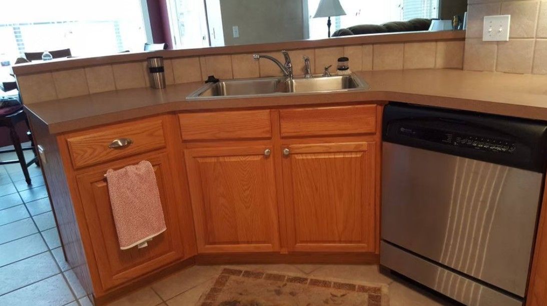 Kitchen sink and wooden cabinets with a dishwasher beneath a countertop and window.