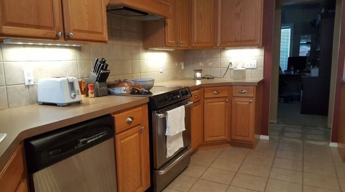 Kitchen with wood cabinets, white countertop, black dishwasher, stove, and tiled floor in warm lighting