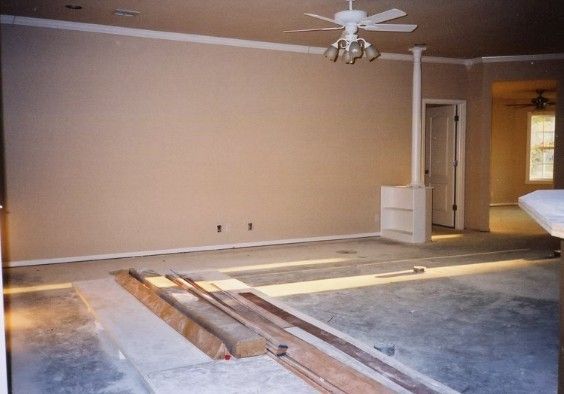 Empty beige bedroom with ceiling fan, scattered floor boards, and a doorway to the hall.