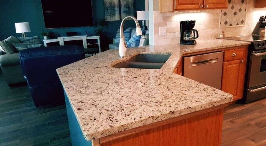 Modern kitchen with granite island, sink, wood cabinets, and a coffee maker in the background.