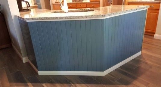 Blue paneled kitchen island with white trim and a wood floor in a bright interior