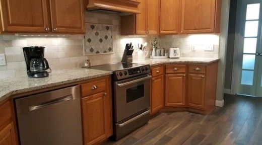 Modern kitchen with wood cabinets, stainless steel appliances, beige counters, and dark flooring
