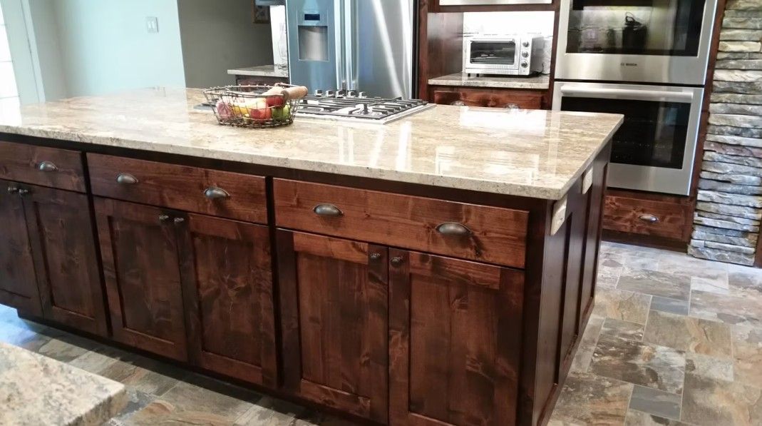 Modern kitchen with a large stone island, dark wood cabinets, and stainless steel appliances.