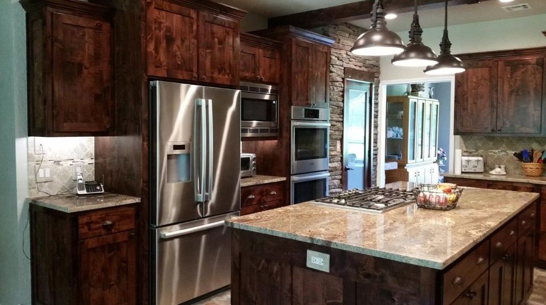 Modern kitchen with dark wood cabinets, stainless steel appliances, and a large granite island under pendant lights