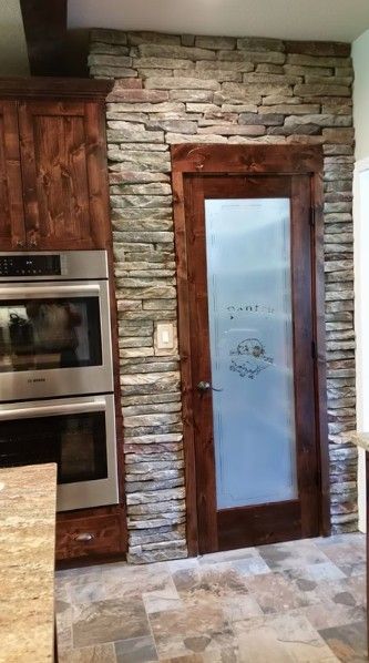 Modern kitchen with stone wall, wood-framed frosted glass door, and built-in stainless steel ovens