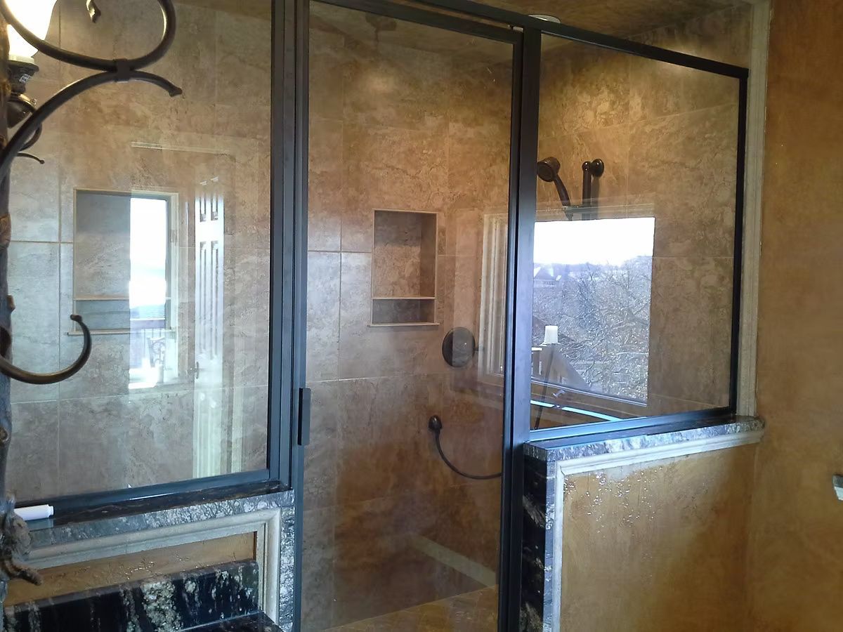Glass shower enclosure in a bathroom with beige tiled walls and chrome fixtures