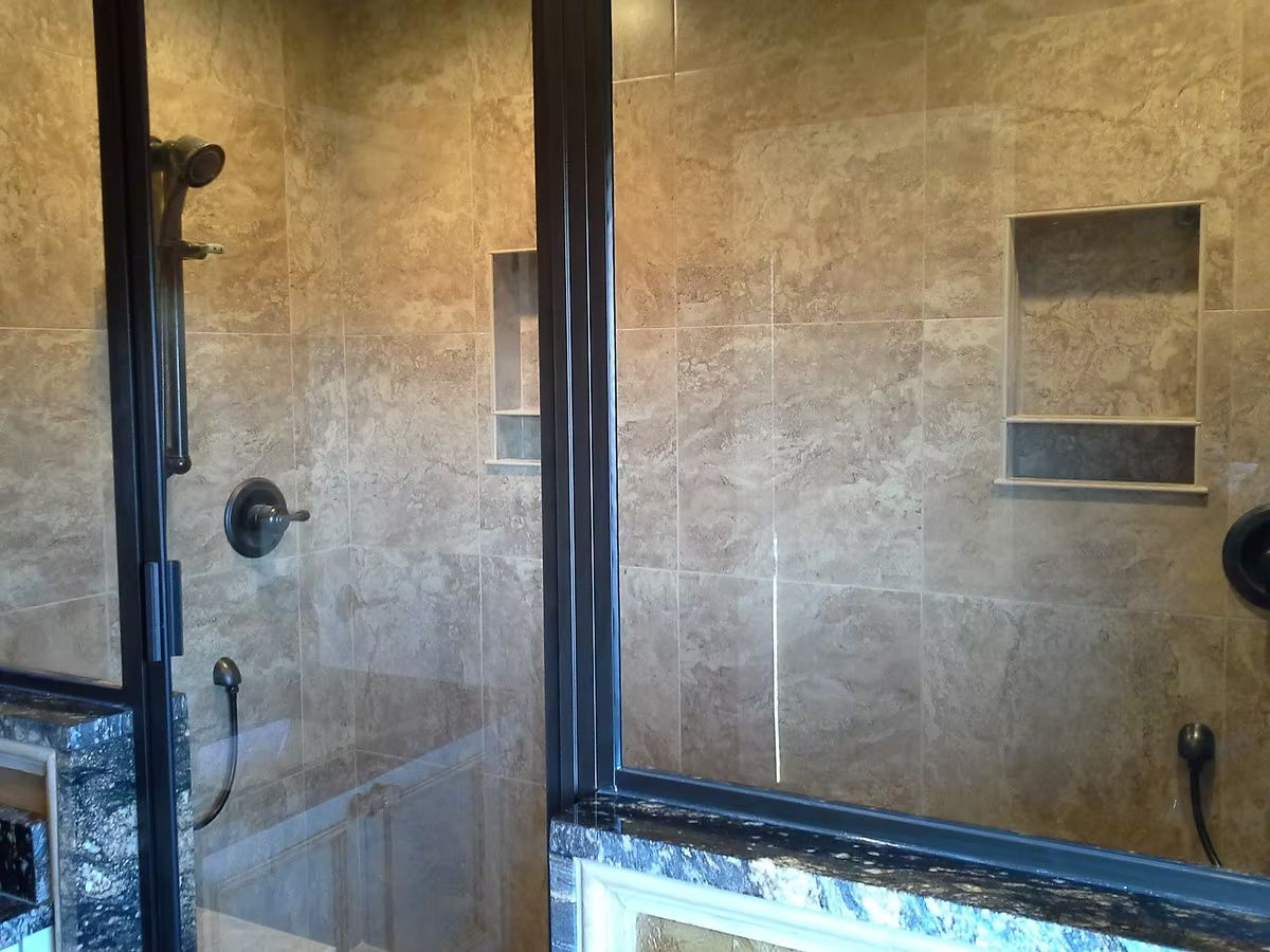 Glass shower with beige tile walls, dark trim, and built-in shelving.
