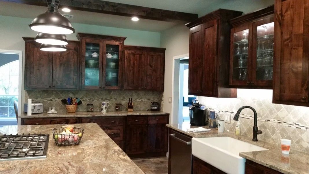 Warm kitchen with dark wood cabinets, granite counters, pendant lights, and a tiled backsplash.