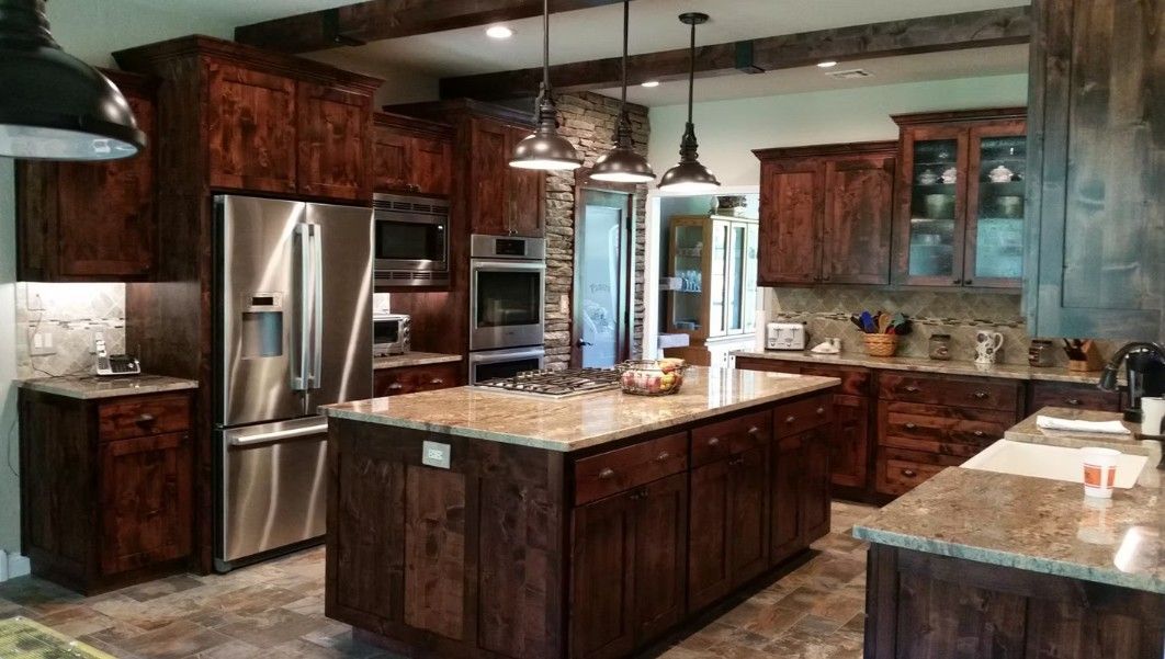 Modern kitchen with dark wood cabinets, granite island, stainless steel fridge, and pendant lights