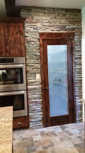 Stone kitchen wall with a wooden-framed frosted glass door beside built-in stainless steel ovens