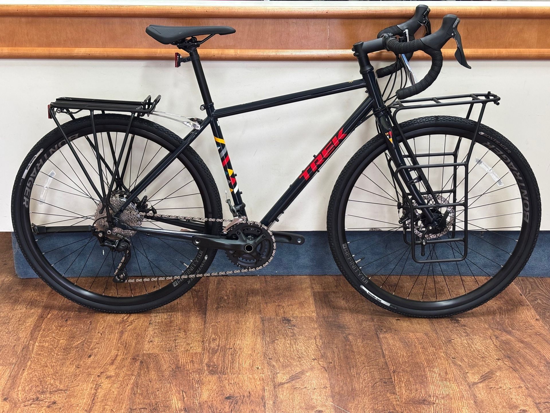 A black bicycle with a rack on the back is parked on a wooden floor.