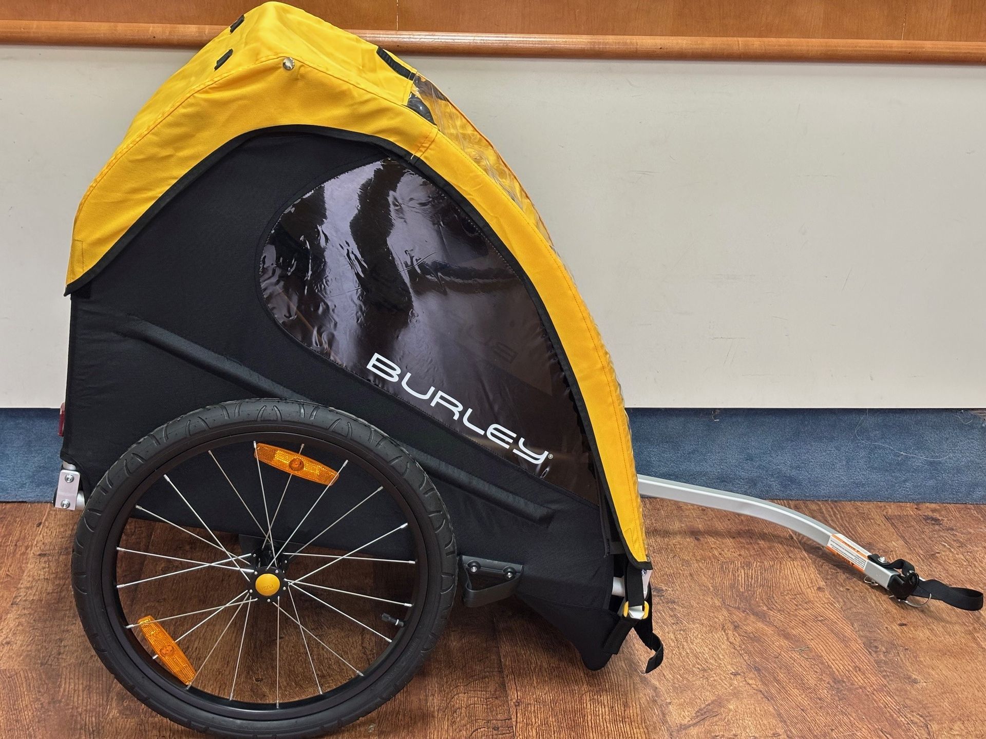 A yellow and black burley bike trailer is sitting on a wooden floor