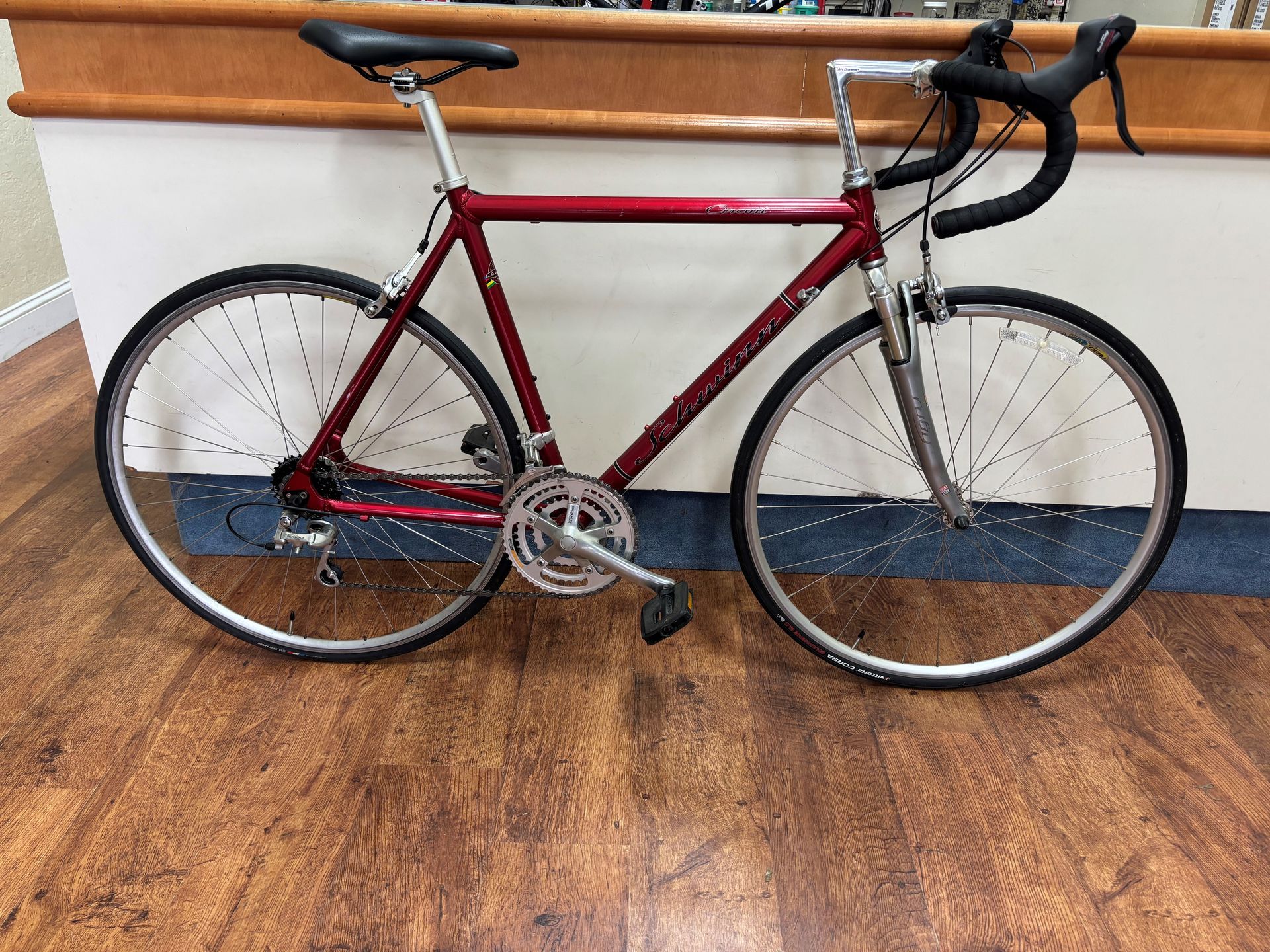 A red bicycle is parked on a wooden floor in front of a counter.