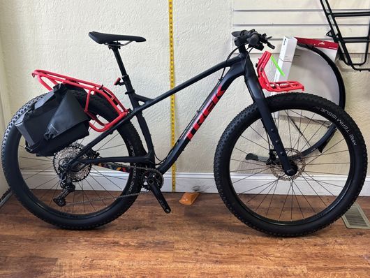 Black Trek bike with red racks, loaded with gear, indoors.