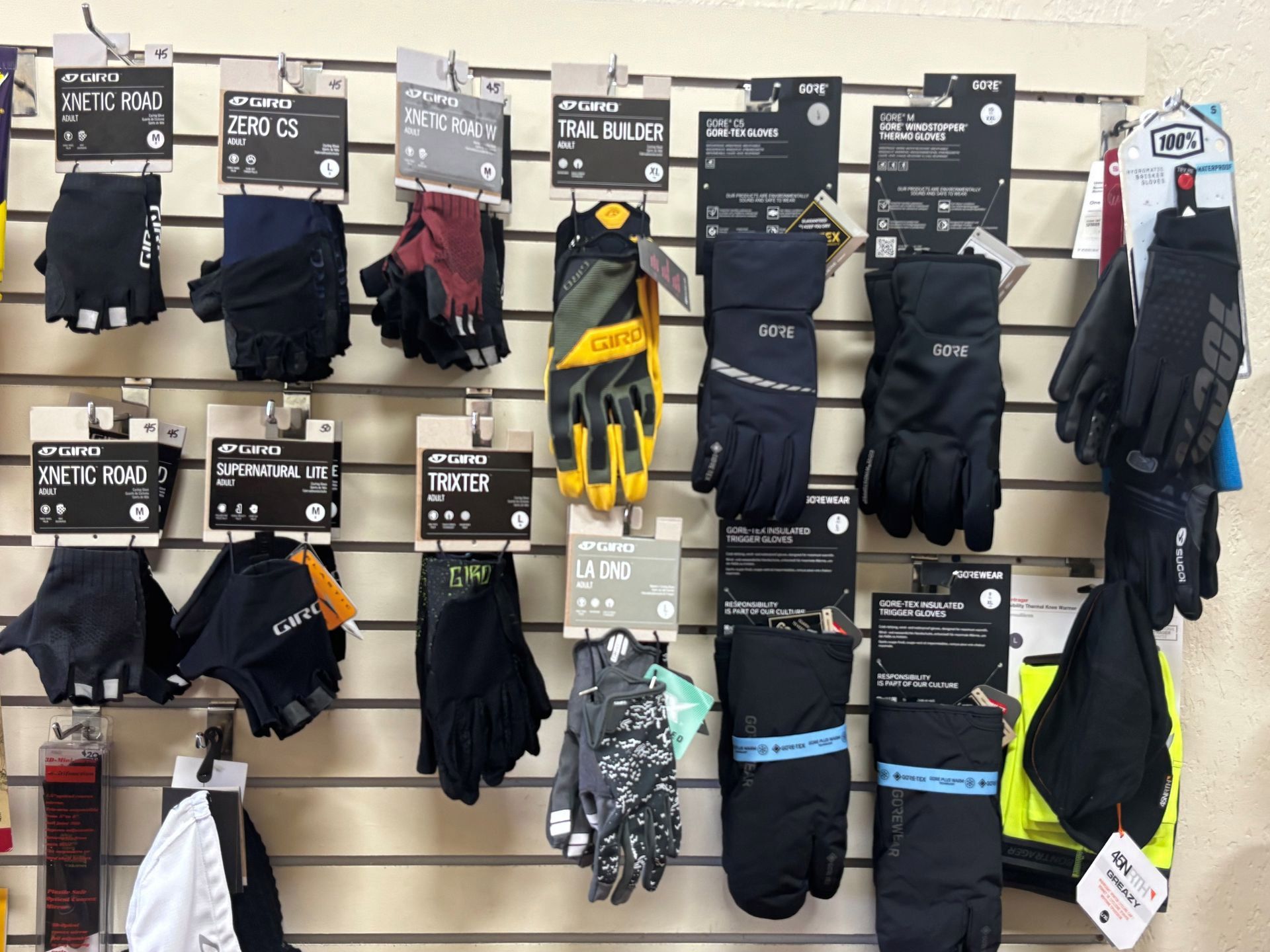 Gloves displayed on a retail wall. Various styles and colors are hanging with price tags.