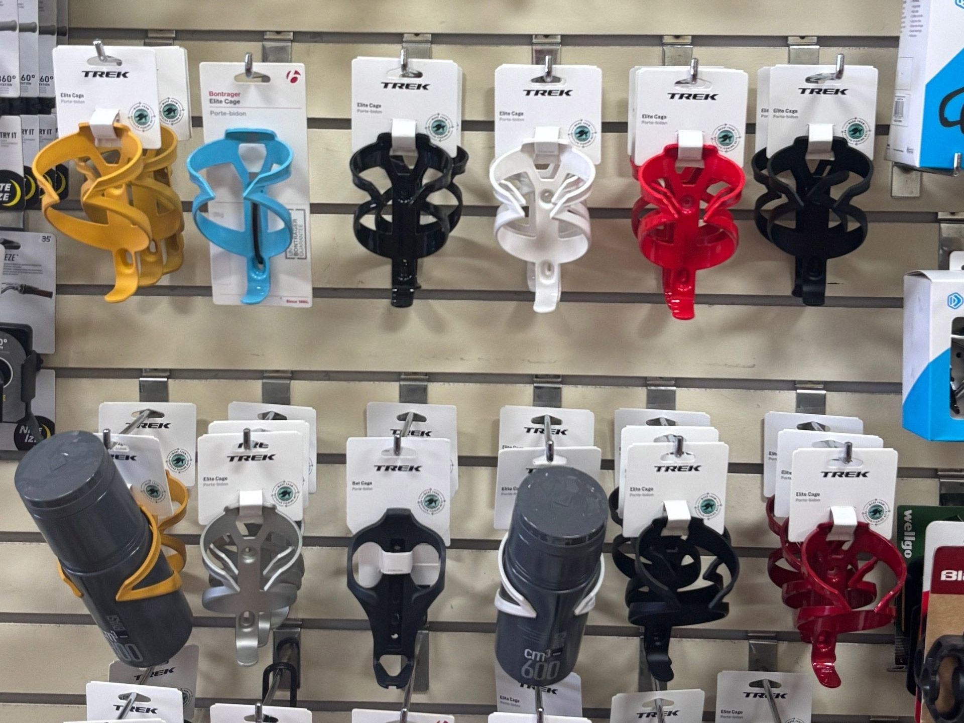 Rows of bicycle water bottle cages on display, various colors: yellow, blue, black, white, and red.