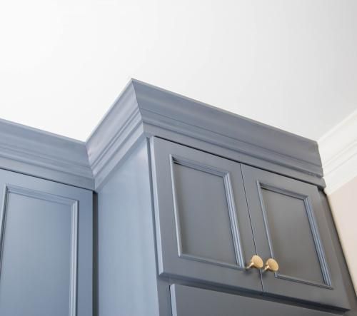 Blue kitchen cabinets with ornate crown molding, set against a white ceiling. Gold cabinet pulls are visible.