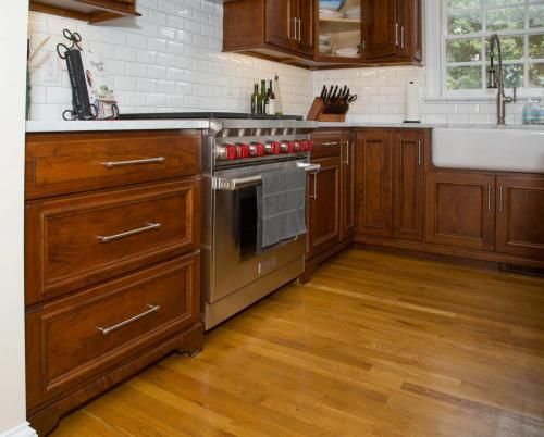 A kitchen with dark wood cabinets, a stainless steel stove, white subway tile backsplash, and light-colored wood flooring.