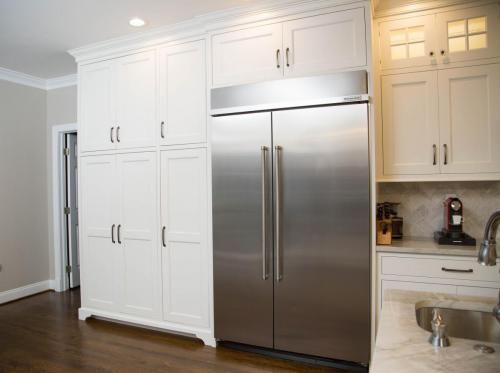 A white kitchen with tall cabinets, a stainless steel refrigerator, and a sink area.