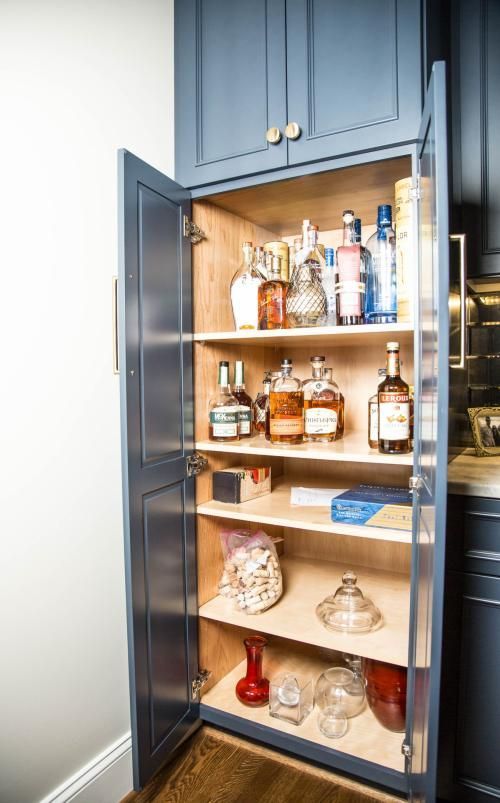 A tall, blue cabinet with open doors revealing shelves filled with bottles, jars, and containers. The interior is light-colored wood.