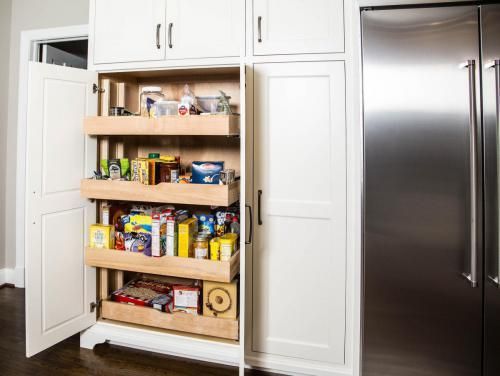 White kitchen pantry with pull-out shelves stocked with food items. Next to a stainless steel refrigerator.
