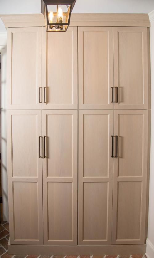Tall, light-colored wooden storage cabinets with dark metal handles. A lantern-style light hangs above.