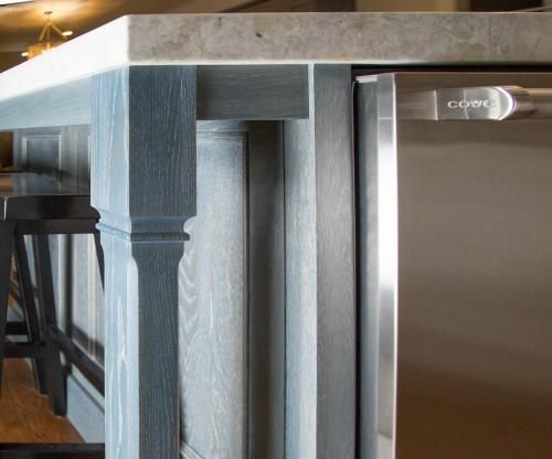 Close-up of a kitchen island with a gray-stained wooden pillar, light gray countertop, and a stainless steel appliance.