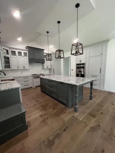 Spacious kitchen with gray cabinets, a large island with a marble countertop, and wood flooring. Three pendant lights hang above the island.