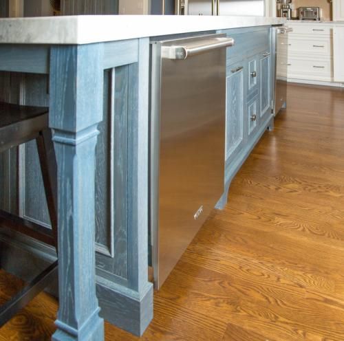 Kitchen island with a blue-gray painted wood frame, stainless steel dishwasher, and white countertop. Rich brown hardwood floors.