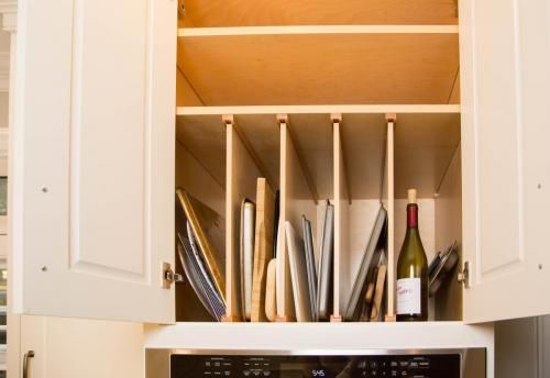 Kitchen cabinet with vertical dividers storing baking sheets, cutting boards, and a wine bottle, above an oven.