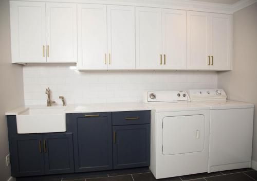 Laundry room with white cabinets, blue lower cabinets, and white appliances; a sink is on the left.