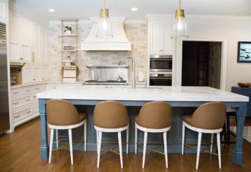 Spacious kitchen with blue island, white cabinets, marble countertops, and four brown and white bar stools.
