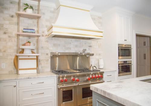 A modern kitchen with white cabinets, stainless steel appliances, and a marble countertop. The backsplash is a light brick.