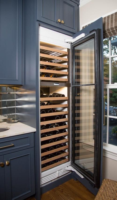 Dark blue kitchen cabinet with a built-in wine cooler holding numerous wine bottles. The cooler door is open, revealing the interior.
