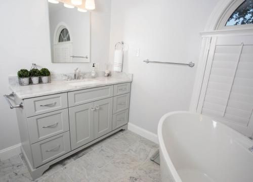 Bathroom with gray vanity, marble countertop, white tub, and window.