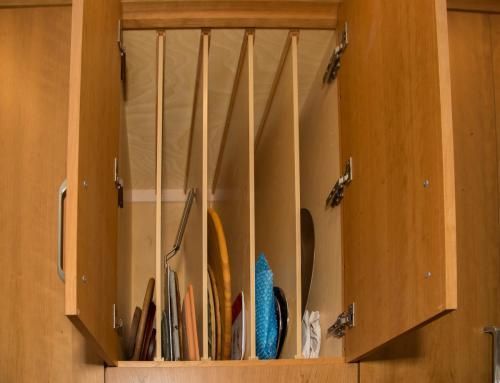 Open kitchen cabinet with vertical dividers, holding plates and utensils. Light wood interior and cabinet doors.