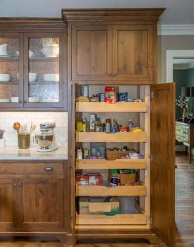 Wooden pantry cabinet open, revealing pull-out shelves stocked with various food items in a kitchen setting.