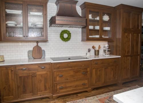 Wooden kitchen with cabinets, range hood, white countertops and backsplash, and a green wreath.