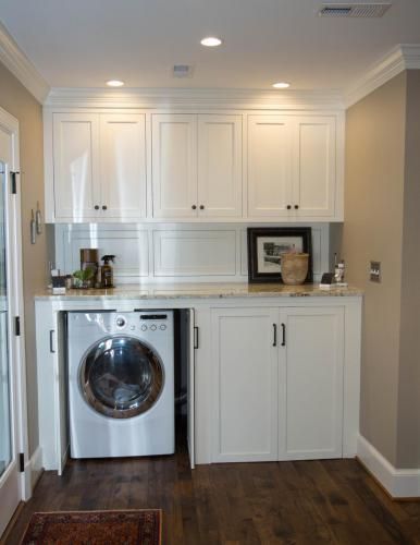 Laundry room with white cabinetry, a front-loading washing machine, and a countertop. The walls are beige, and the floor is dark wood.