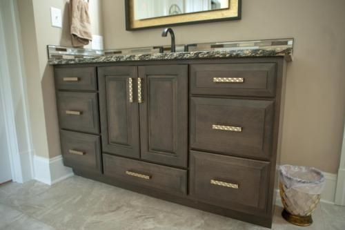 Gray bathroom vanity with drawers and cabinets, topped with a speckled countertop, near a wastebasket.