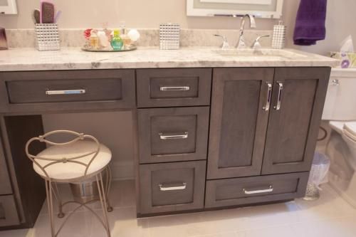 A dark gray bathroom vanity with chrome hardware, a light granite countertop, and a small stool in front.
