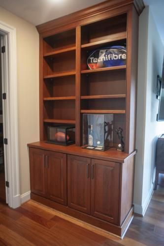 Wooden built-in bookcase with upper shelves and lower cabinets; displayed items include a tennis racquet, memorabilia, and a microwave.