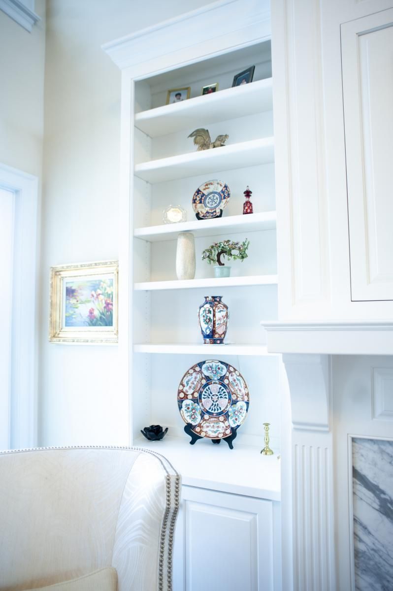 Built-in white bookshelf filled with decorative items next to a wall with a framed painting.