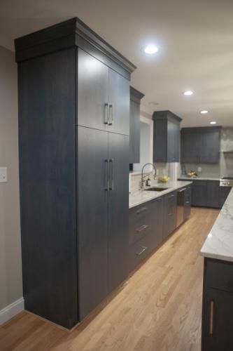 Navy blue kitchen cabinets with silver hardware in a modern kitchen.  Light wood flooring and a white countertop.