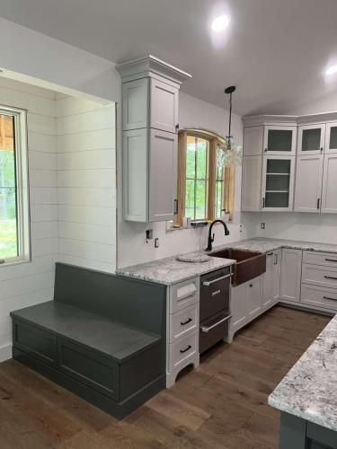 Gray and white kitchen with a built-in bench, cabinets, and a copper sink. The window has a wooden frame.